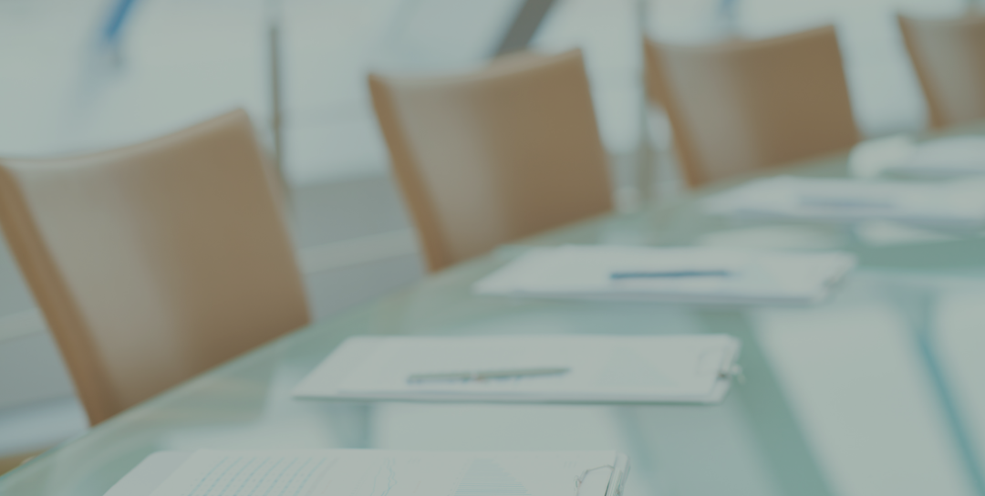 Image of office meeting room table with chairs and clipboard and pens laid out ready for people to attend