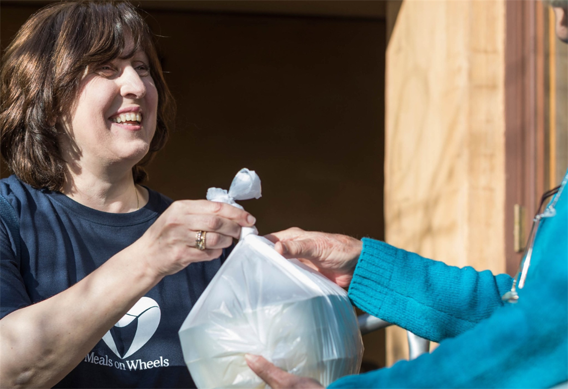 Meals on wheels team member handing over food to person