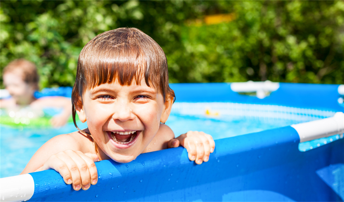 Young boy holds onto side of non-compliant portable pool grinning at camera