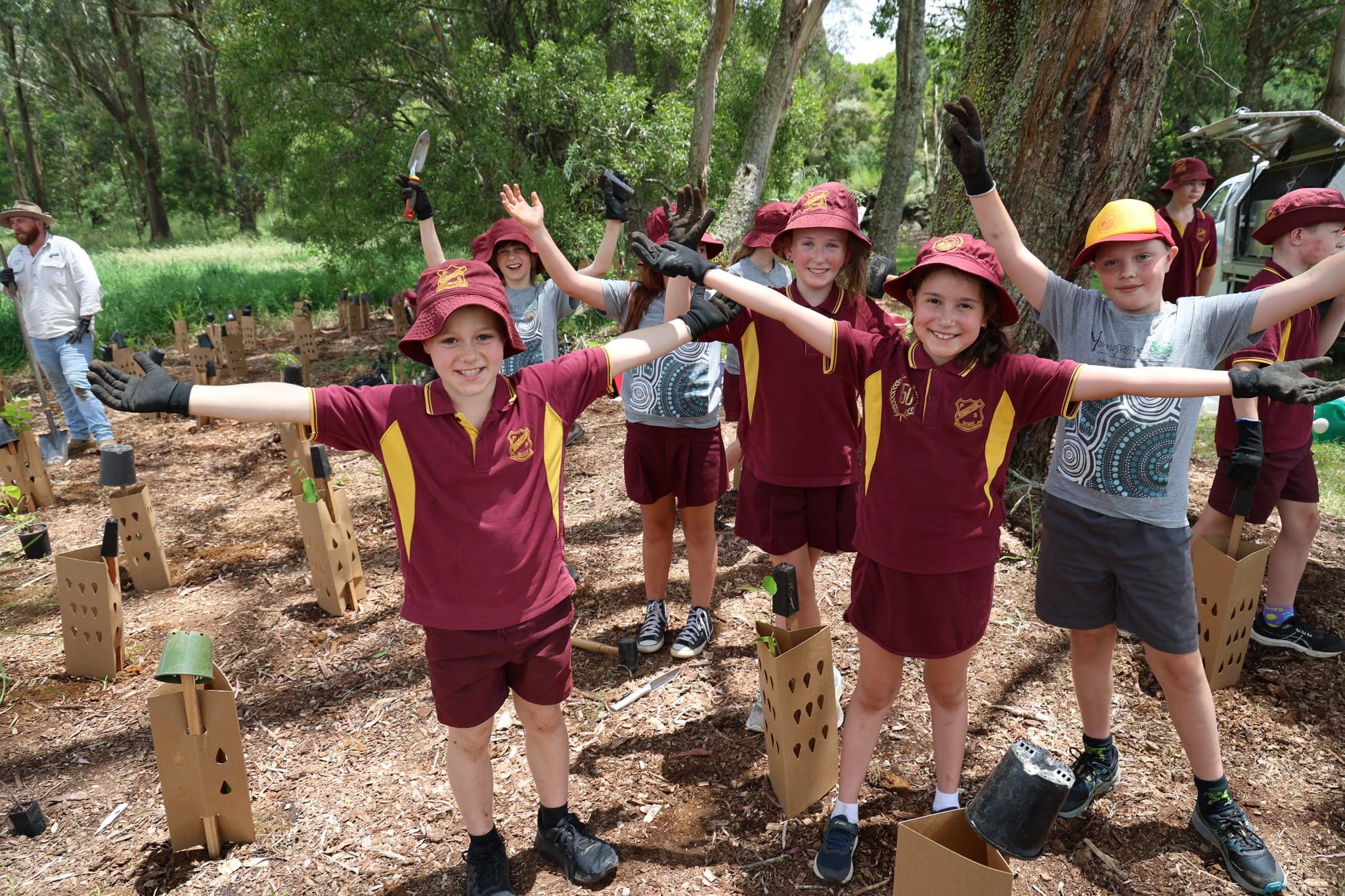 A small group[ of Robertson Puplic School students hold out their arms smiling at tree planting site