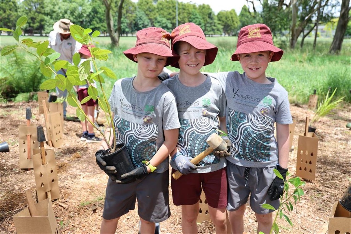 Three Roberston Public School Students holding during planting day holding tubestock trees