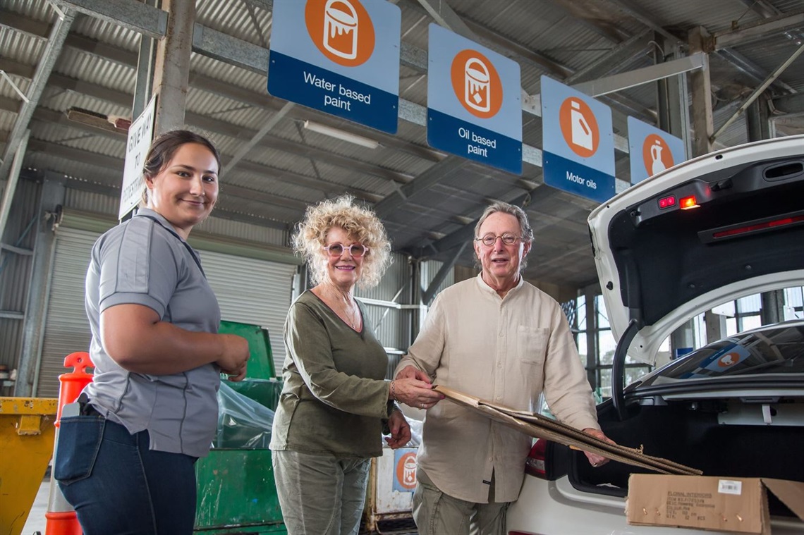 A man and woman stand next to open car boot open to drop off waste at the community recycling centre with staff member 