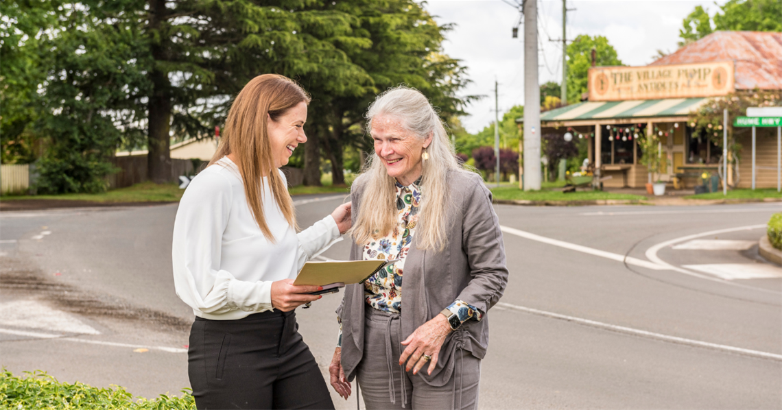 Two ladies standing on street, laughing and discussing village plans