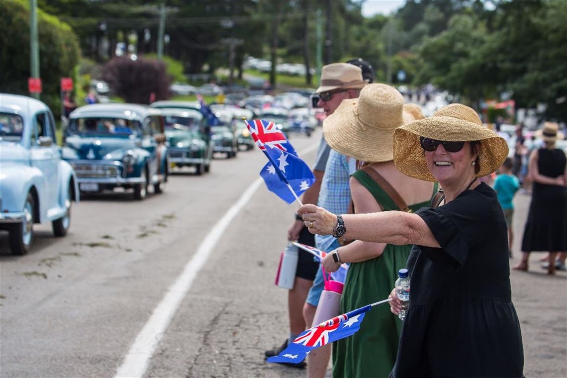 Woman smiles and waves Australian Flag as fleet of classic cars drives by in the Australia Day Grand Parade. Photo by Neil Fenelon.