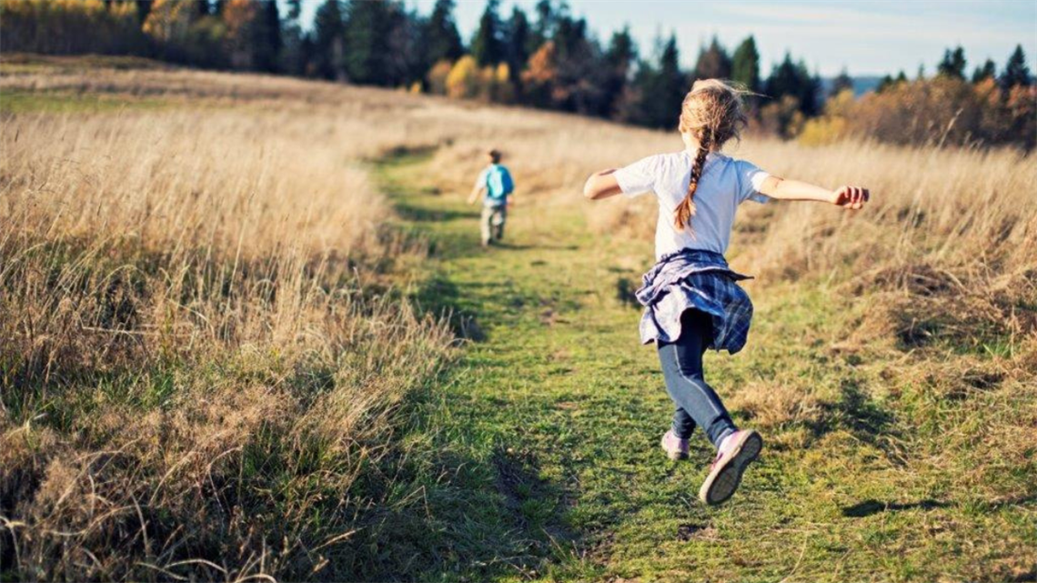 2 kids running across a paddock that is clear of rubbish