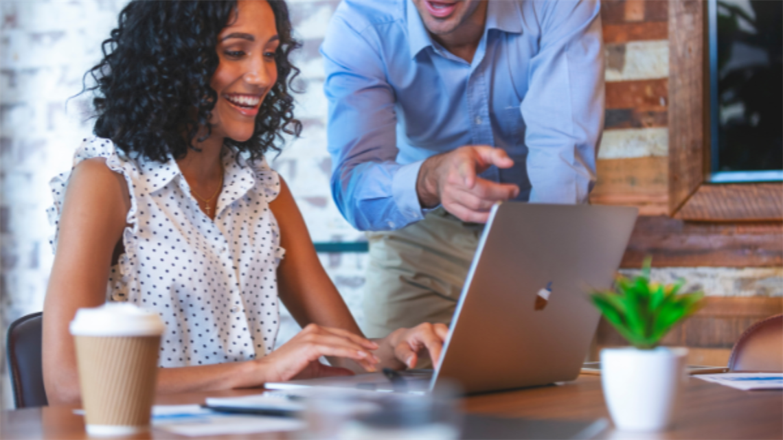 Lady on her laptop and a colleague leaning over pointing at something on the screen