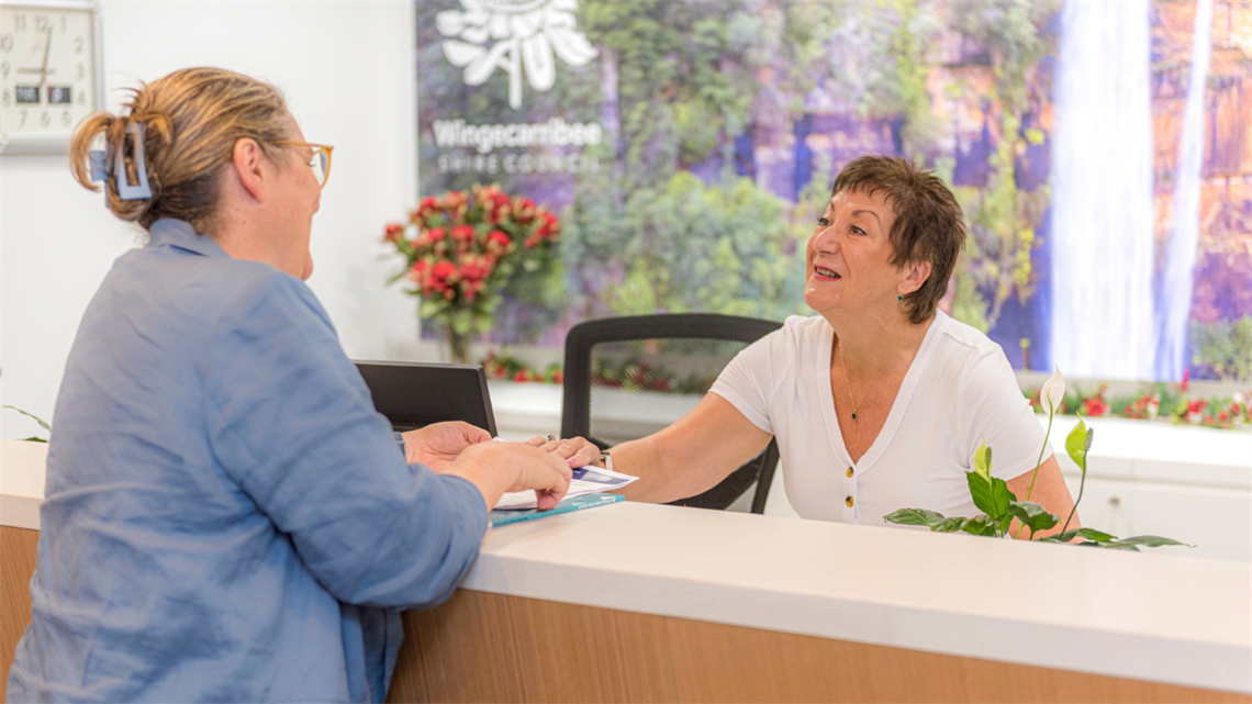 Customer service council staff leaning on counter and talking to a customer