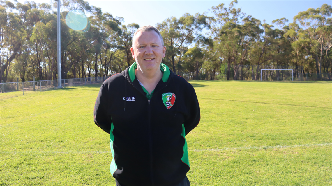 Man standing on soccer field, smiling to camera