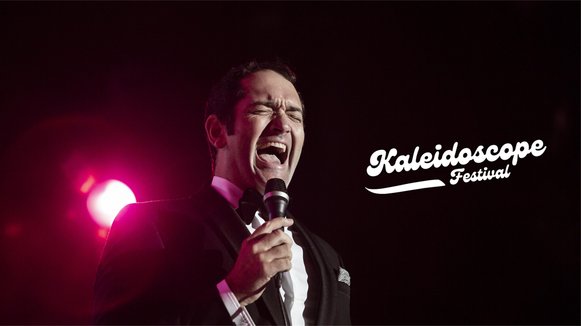 Close-up of Darren Percival in black suit sings on stage. Text reads Kaleidoscope Festival 