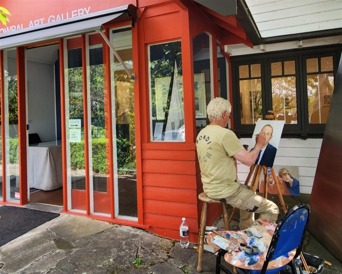 Front entrance of Bowral Art Gallery, red cottage style studio. A man with easel paints a portrait outside