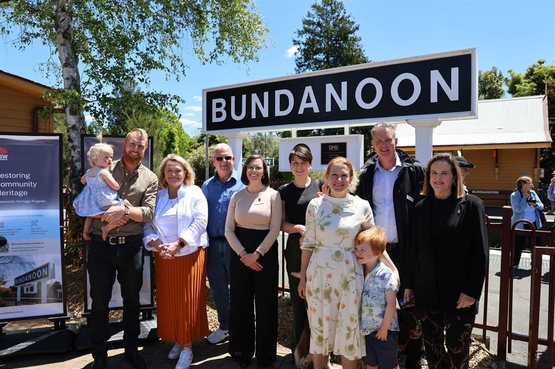 Mayor Jesse Fitzpatrick, Wendy Tuckerman, Cr Farrell, Cr Duffy, Cr Champion, Cr Russell and Cr Kent and Anna Watson stand in front of Bundanoon Station sign