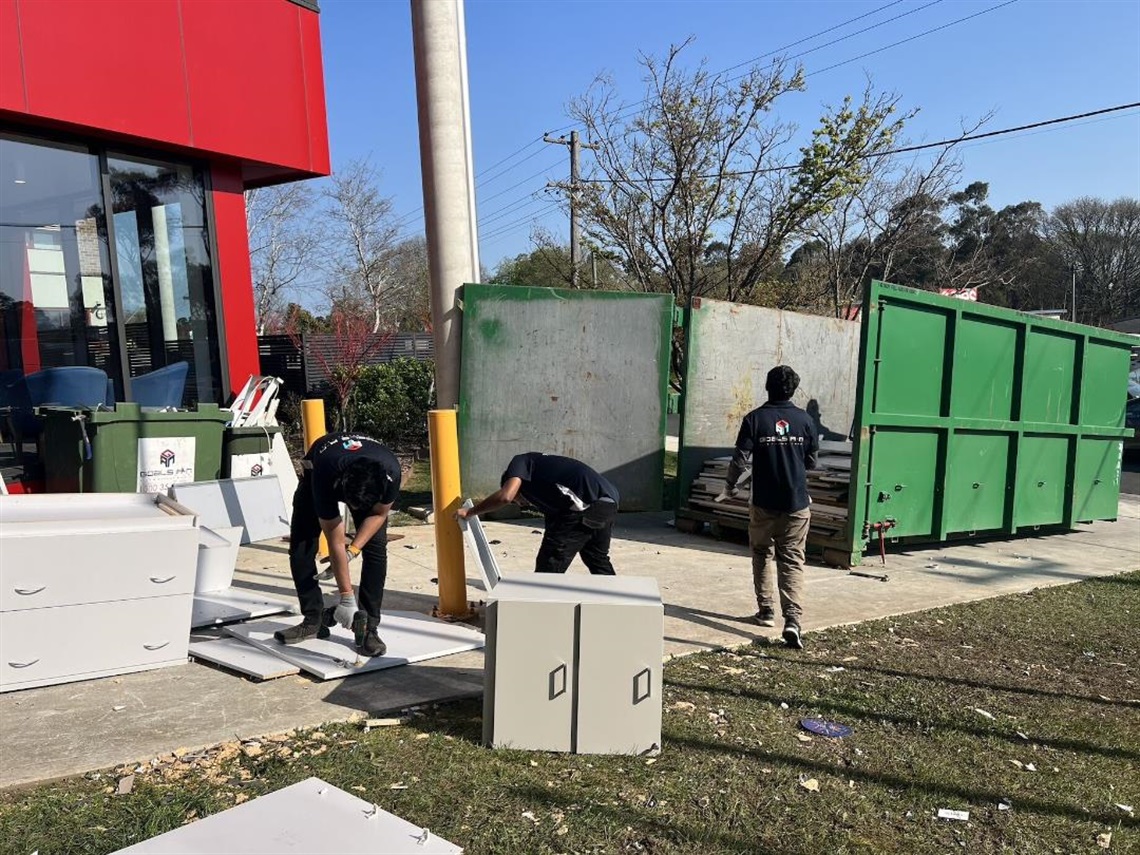 Three workers from Green Furniture Hub breakdown office furniture and add to skip recycling bin for resource recovery