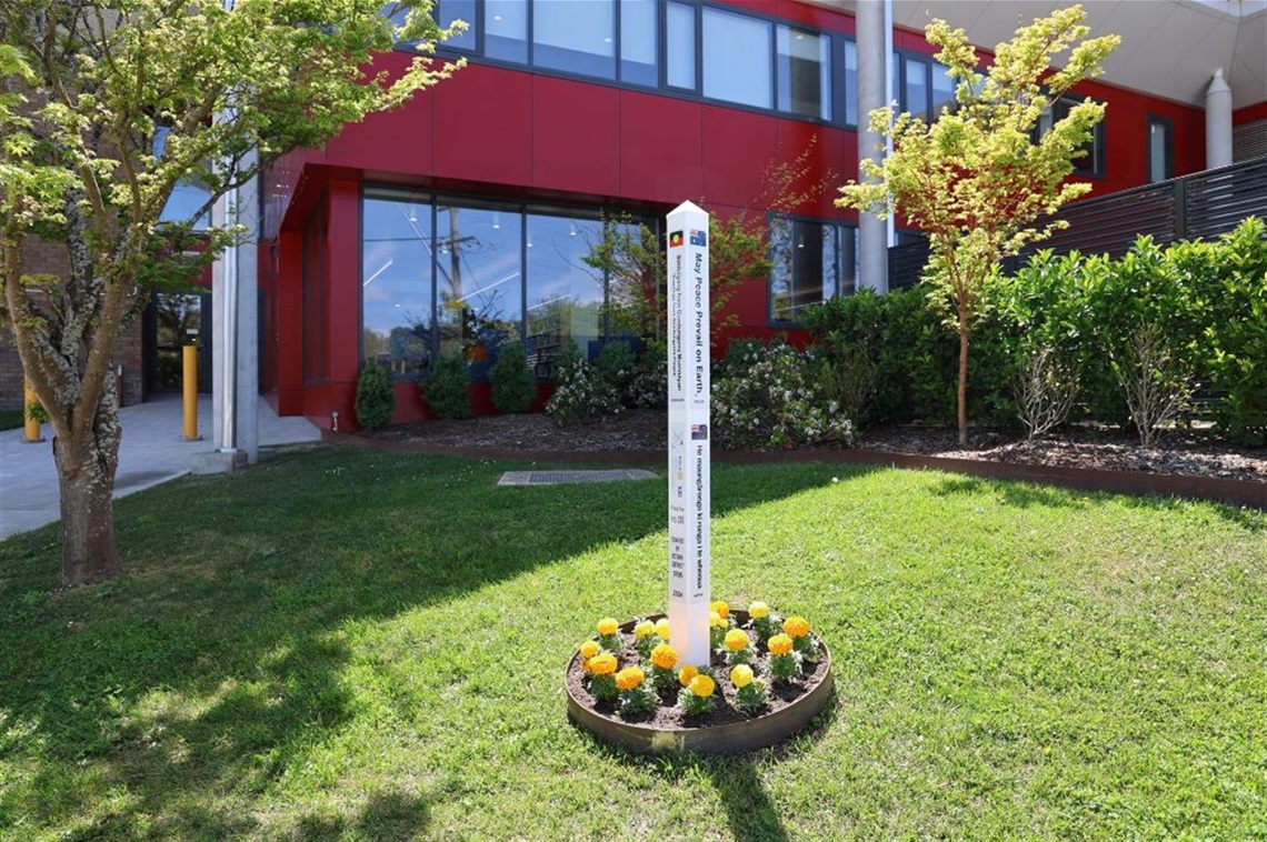 White Peace Poll in round garden bed with Civic Centre in background, visible text 