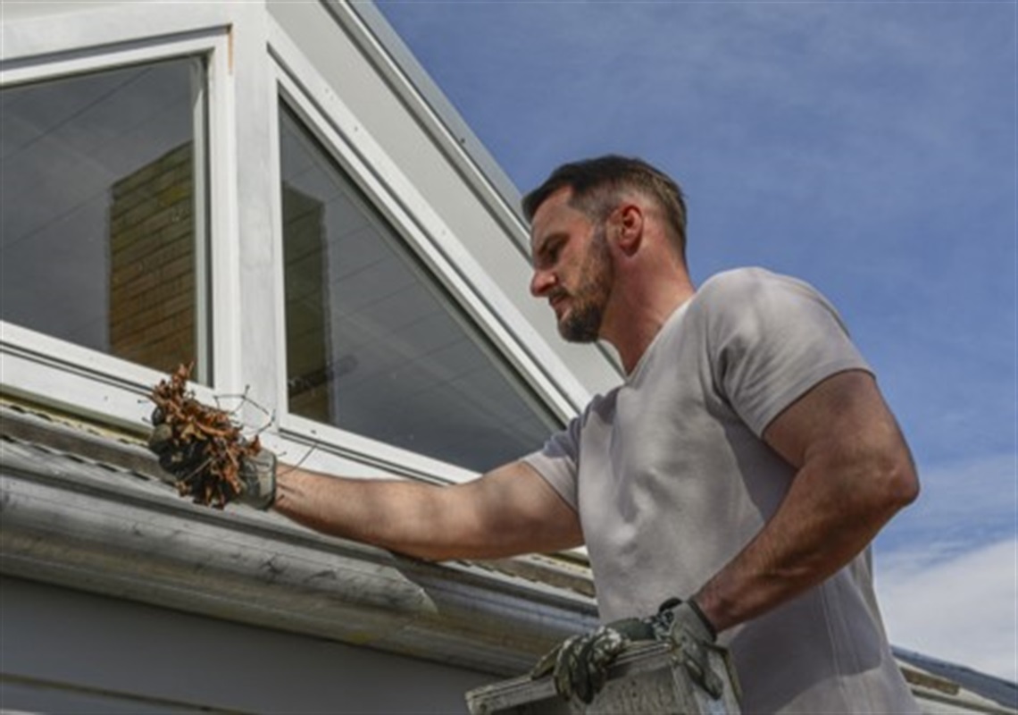 man cleaning leaves from roof gutter